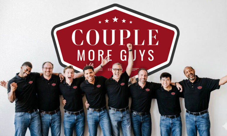 Eight men in matching black polo shirts and jeans stand smiling with arms around each other in front of a large red and white sign that reads “COUPLE MORE GUYS.”.