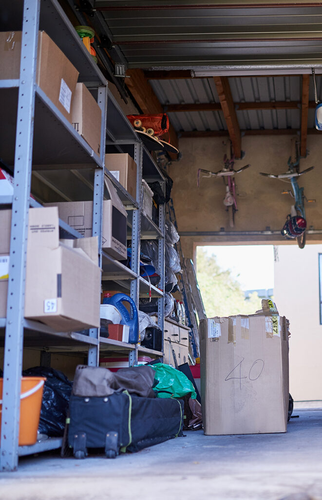 A garage with metal shelves holding boxes and various items, a large cardboard box labeled “40” on the floor, and two childrens bicycles hanging from the wall in the background.