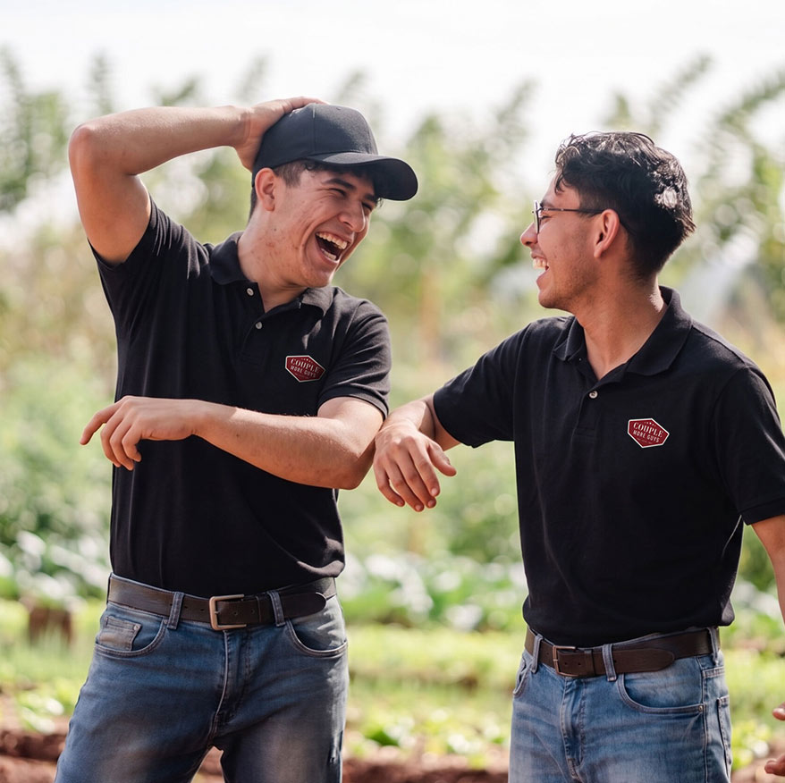 Two men in black polo shirts and jeans laughing together in a field.